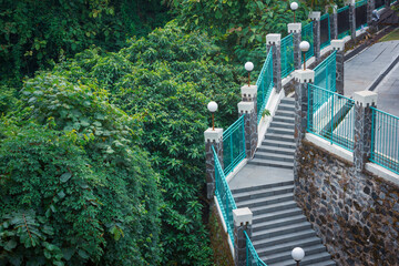 Top view of stairs with steel fence, round lamps and stone wall decoration, side of cliff with many trees