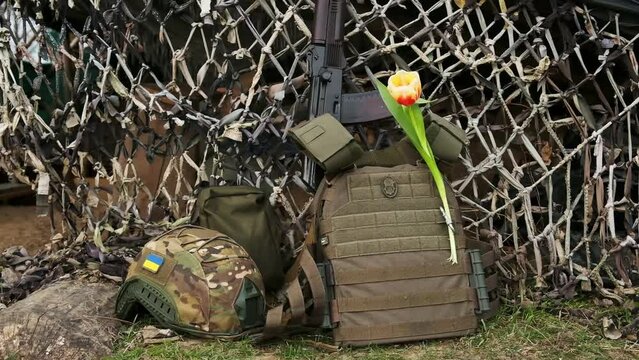 a man's hand puts a tulip in a bulletproof vest near a weapon. a composition from the ammunition of a Ukrainian soldier with a red tulip.