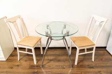 Fototapeta premium A table and two chairs are set up in a room. The table is made of glass and has a round shape. The chairs are white and have a woven design