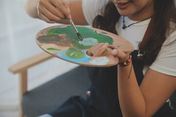 Cropped image of female artist standing in front of an easel and dipping brush into color palette