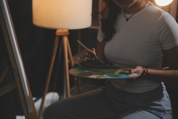 Cropped image of female artist standing in front of an easel and dipping brush into color palette