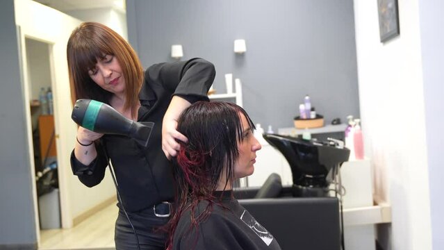 Hairstylist drying the hair of a woman in front of a mirror in the salon