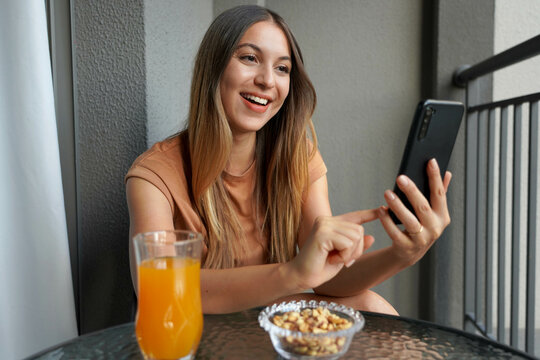 Laughing attractive Brazilian girl sends messages with smartphone chatting app on balcony in her apartment. Time to relax.