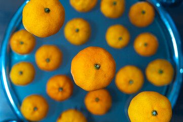A close up of many mandarins on a blue background. The mandarins are all different sizes and are arranged in a circular pattern. Concept of abundance and freshness, as well as a feeling of warmth and 