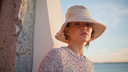 Calm tourist posing seashore in evening closeup. Peaceful beautiful girl in hat