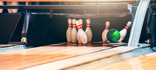 Bowling ball hits pins at end of glossy wooden bowling alley.  - obrazy, fototapety, plakaty
