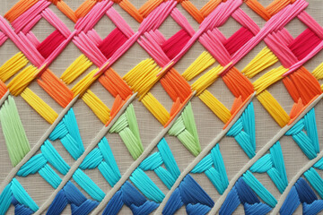 A close-up of colorful decorative embroidery as a background. Stitches of yellow, blue and pink creating an abstract pattern on grey canvas. AI-generated