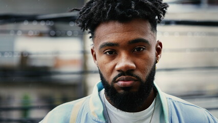 Portrait of a young black man with solemn expression standing outside in drizzle rain looking at...