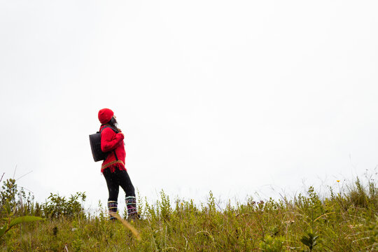 Explorando el invierno Chica con mochila y chompa rojo disfrutando del paisaje campestre bajo un cielo nublado,turista viajero,estilo de vida