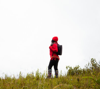 Explorando el invierno Chica con mochila y chompa rojo disfrutando del paisaje campestre bajo un cielo nublado,turista viajero,estilo de vida