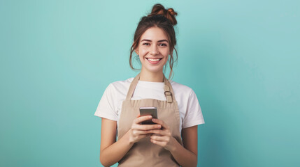 Young woman in apron engaged with smartphone against teal background