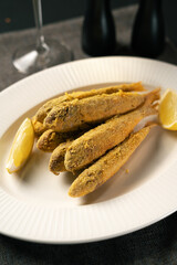 Mullet fish fried in breadcrumbs served on a white plate with wine in the background. Restaurant menu concept.