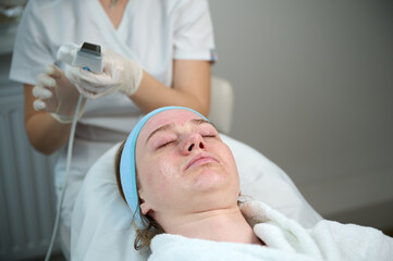 Close up of ultrasound skin cleaning and facial peeling procedure in beauty clinic. Macro shot of...