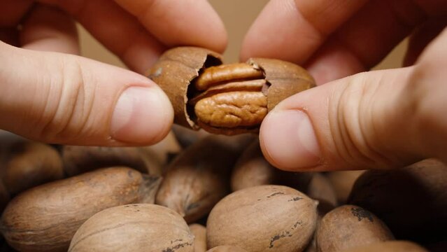 Men's hands crack the shell of a pecan into two parts and examine the nut inside. Close-up, plate with nuts.