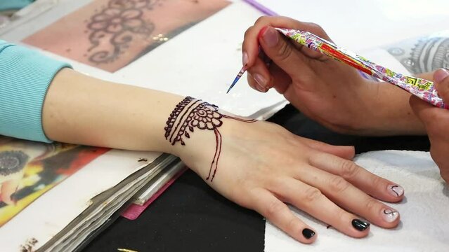 Artist carefully applies intricate henna designs to a client's wrist, showcasing the detailed process of this traditional body art