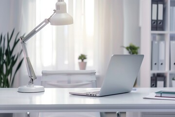 White desk with laptop, table lamp, stationery and decor over blurred background modern office .