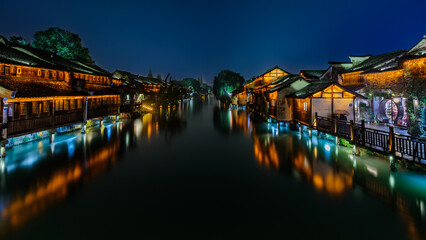 Attractive night scenery of traditional Chinese houses on both banks of a canal in a chilly and rainy evening at the ancient township of Wuzhen near Shanghai, China.