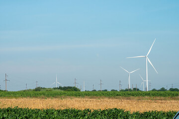 Windmills with spinning rotor blades generate energy on harvested yellow field under blue sky....
