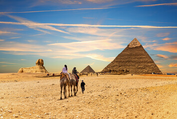 Tourists on camels with bedouin in front of the Great Pyramids of Egypt, Giza