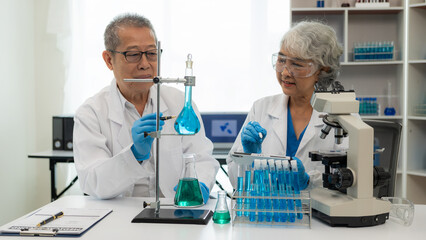 test tube microscope Two senior clinical workers, two men and women in the laboratory, two scientists doing research, young woman and her senior supervisor investigating with microscope and laptop.