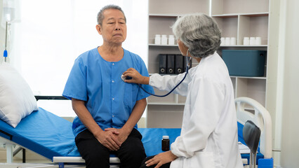 Senior female doctor uses stethoscope to check heartbeat. Senior man listens to heartbeat using...