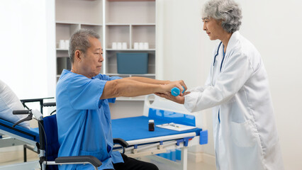 Obraz premium An elderly Asian man is doing physical therapy with the support of an elderly female nurse using dumbbells and tubes to exercise for a patient.