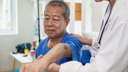 An elderly Asian man is doing physical therapy with the support of an elderly female nurse using dumbbells and tubes to exercise for a patient.