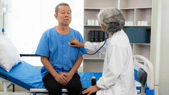 Senior female doctor uses stethoscope to check heartbeat. Senior man listens to heartbeat using stethoscope at hospital for checkup. Elderly health care concept.