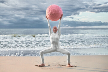 Hairless performer girl with alopecia in white futuristic suit dancing with pink sphere at sea,...