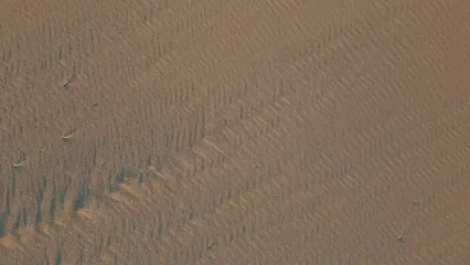 Fototapeten Sandy sunset beach texture top view. Aerial zoom out wind marks on wet sand © stockbusters