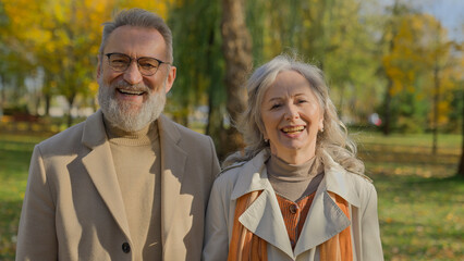 Portrait of happy mature couple smiling in autumn park cheerful old woman man posing together for camera in nature outdoors elegant senior husband wife retired family laugh have fun love relationship