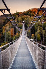 The warm, late-afternoon sun casts a golden glow over an empty suspension bridge, framed by the fiery colors of fall foliage, inviting a tranquil walk