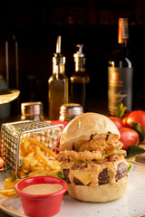Surf and turf seafood and meat burger with fried squid rings, melted cheese, crispy bacon and a beef patty served on a wooden board with side potato