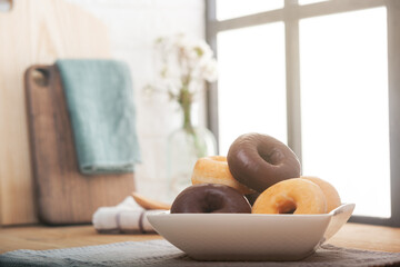 Doughnuts piled up on a plate. Background of a window illuminating the kitchen worktop.