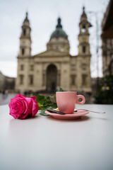 A pink rose and a coffee cup on a table in front of basilica