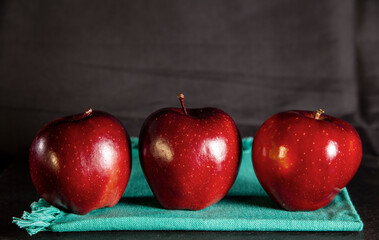 Three red apples on a green napkin and a black background