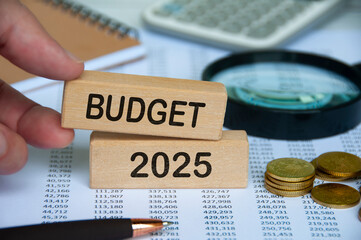 Fototapeta premium Hand holding wooden block with text - Budget 2025 with financial data background. Budgeting concept