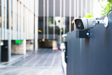 A modern security camera attached to a building's exterior wall, overseeing a blurred entrance...