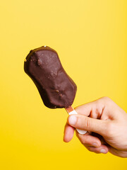 Chocolate ice cream stick in hand isolated on yellow background