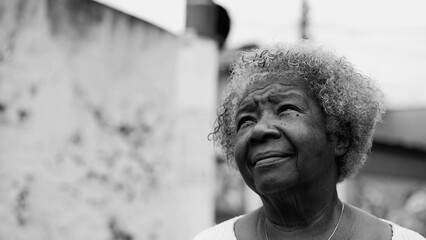 One contemplative wise senior African American woman standing urban street gazing skywards in...