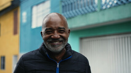 Obraz premium One joyful South American black man standing in urban street smiling at camera, close-up face in tracking shot and cityscape backdrop