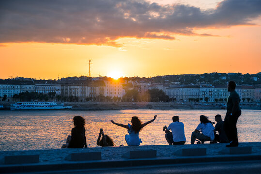 Group Of People Watching Sunset By The River In The City