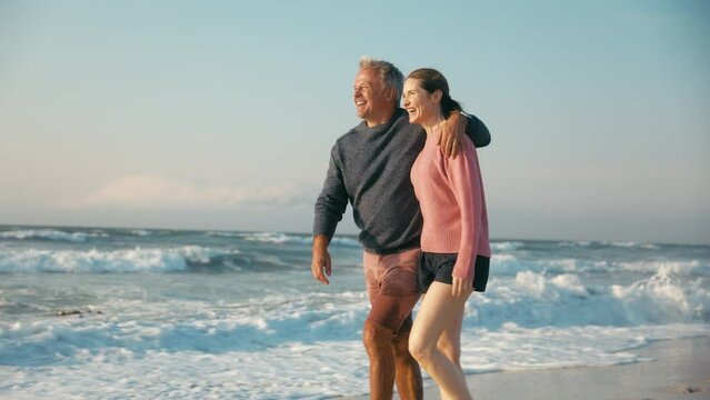 Camera tracks loving retired senior couple on vacation walking on beach shoreline hugging at sunrise -  shot in slow motion