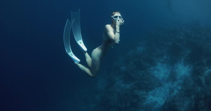 Woman freediver dives to the deep in blue ocean and equalizes pressure.