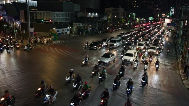 Motorcycles and cars navigate through a bustling central intersection in Bangkok, showcasing the vibrant night-time city traffic and urban life in Thailands capital.