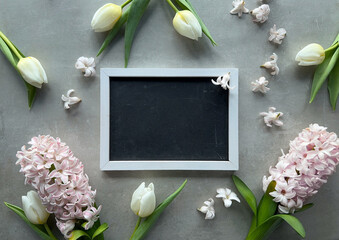 A wooden picture frame placed on a table, encircled by fragrant spring flowers, white tulips and pink hyacinth.