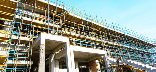 A building under construction with scaffolding and a yellow and blue ladder. The building is in the process of being built and is not yet finished