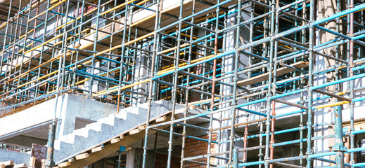 A building under construction with scaffolding and a staircase. The scaffolding is blue and yellow