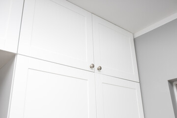 A cabinet under the ceiling for storing boxes and shoes. Round handles of a white cabinet. Stylish...
