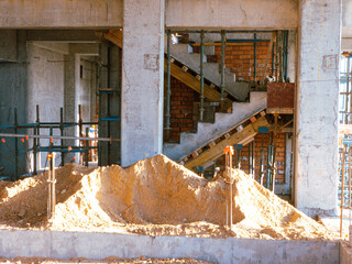 A pile of dirt is in front of a building. The dirt is piled up in a mound, and it is surrounded by scaffolding. The building is under construction, and the dirt is being used to level the ground